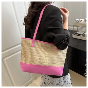 Detail of handwoven straw tote bag with vibrant pink leather handles on model shoulder