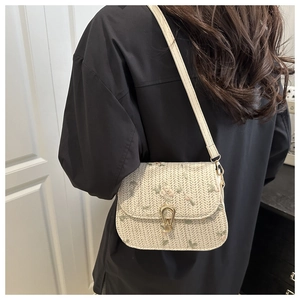 Detail of cream straw saddle bag with floral embroidery and gold buckle on a model