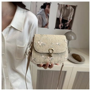 Detail of beige straw crossbody bag with floral embroidery and golden metal clasp