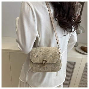 Detail of straw woven saddle bag featuring floral embroidery and leather shoulder strap