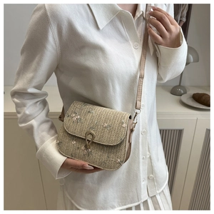 Detail of woven straw shoulder bag with delicate pink floral embroidery and metal buckle