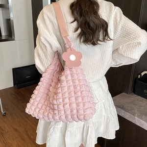 Sac à bandoulière rose à texture gaufrée avec breloque fleurie porté par un mannequin