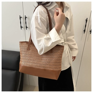 Detail of handwoven straw tote bag with brown leather handles worn by a model
