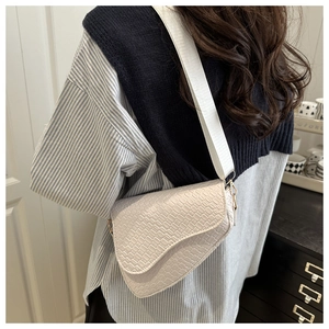 Detail view of white crocodile pattern saddle bag with wide strap on striped shirt