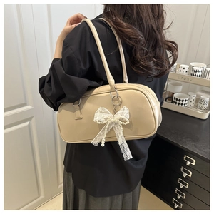 Close-up of cream shoulder bag with lace bow and pearl charm worn by a model