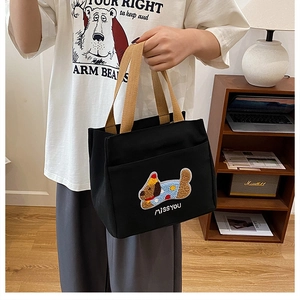 Détail du sac en toile noire avec broderie de chien en 3D et poignée tissée brune