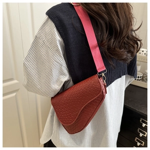Detail of red-brown saddle bag with woven texture and pink adjustable strap