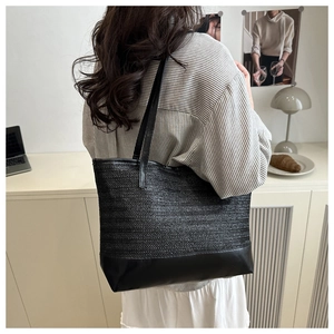 Detailed view of woven straw tote bag with black leather straps on a fashion model shoulder