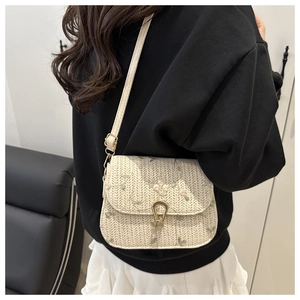 Close-up of cream woven crossbody bag with floral embroidery and gold horseshoe lock
