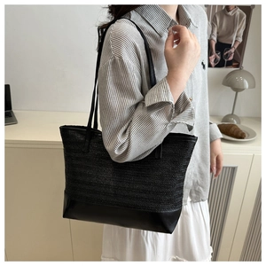 Detail of woven straw tote bag with black leather patchwork on model in home setting