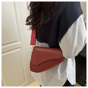 Detail of burgundy saddle bag with crocodile texture and wide textile strap on model