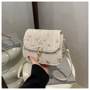 Detail of woven straw crossbody bag with floral embroidery and gold metal clasp