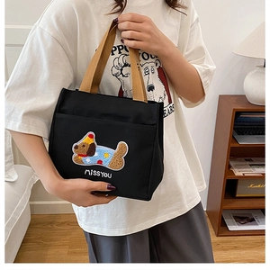 Gros plan d'un sac à lunch en toile noire avec broderie chiot et poignée marron