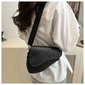 Close-up of black crocodile-embossed saddle bag with wide strap on a model