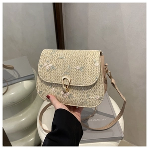 Close-up of woven straw bag with floral embroidery and gold metal clasp lock