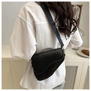 Detailed view of a black woven saddle bag featuring a wide fabric shoulder strap worn by a model