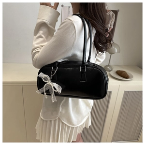 Detail of black leather shoulder bag featuring a lace bow charm with pearl accent