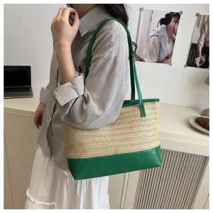 Detail of woven straw tote bag with green leather trim worn by model in casual setting