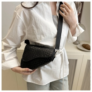 Detail of black saddle bag with woven texture and gold metal hardware on wide strap
