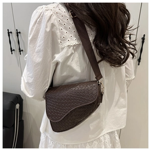 Detail of a dark brown woven saddle bag featuring gold hardware and a vintage casual style