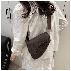 Detail of dark brown croc-embossed saddle bag with wide canvas strap and gold buckle