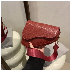 Close-up of burgundy crocodile pattern saddle bag with wide fabric strap and gold hardware