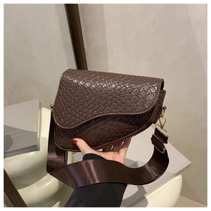 Close-up of a dark brown saddle bag with woven texture and a wide nylon shoulder strap