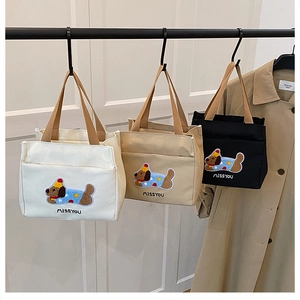 Trois sacs en toile avec broderie de chien suspendus devant un manteau beige