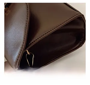 Gros plan des coutures du cuir marron foncé et des ferrures dorées du sac à main
