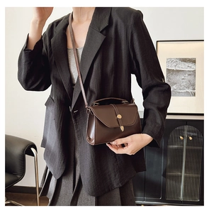 Détail d'un sac bandoulière marron foncé structuré avec fermoir doré sur modèle