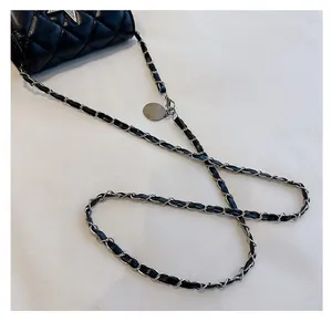 Detail of silver chain strap with black leather weave and round metal pendant on a quilted bag