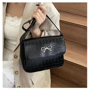 Détail du sac noir à texture crocodile avec nœud doré porté sur un tailleur beige