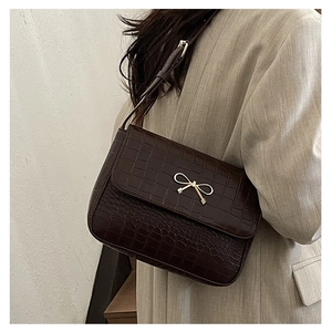 Détail du sac à main marron foncé effet crocodile avec nœud doré porté par un modèle
