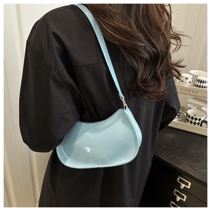 Détail du sac croissant en cuir verni bleu clair porté à l'épaule sur un haut noir