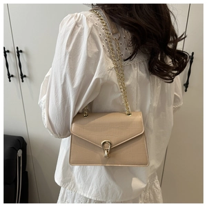 Detail of beige crocodile pattern handbag with gold chain strap and shield clasp