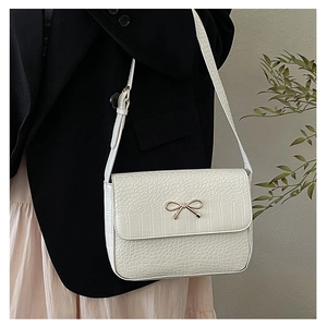 Détail du sac bandoulière blanc à texture crocodile avec boucle nœud doré sur un mannequin