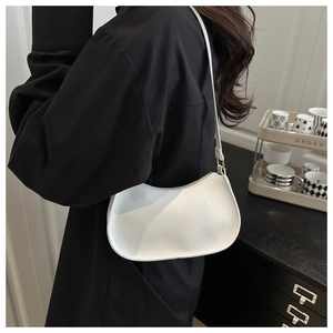 Sac à bandoulière minimaliste en cuir verni blanc porté à l'épaule en situation réelle