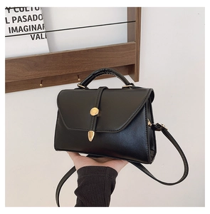 Détail du sac bandoulière noir avec boucle dorée ronde et rabat en forme d'enveloppe