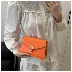 Detail of bright orange crocodile-embossed bag with gold U-shaped metal lock and chain