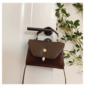 Détail d'un sac bandoulière trapèze marron foncé avec fermoir doré sur une poignée de porte