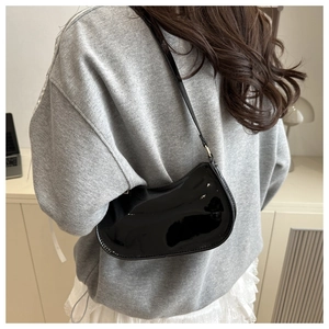 Sac bandoulière en cuir verni noir brillant porté par un mannequin dans un bureau à domicile
