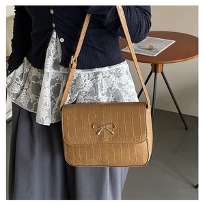 Sac bandoulière marron effet crocodile avec fermoir nœud doré sur bureau en bois