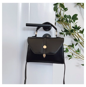 Détail d'un sac bandoulière en cuir noir avec boucle dorée en C sur une porte blanche