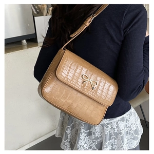 Détail du sac à bandoulière en cuir croco avec nœud doré porté au dos par un mannequin