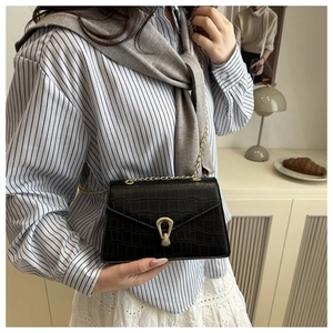 Detail of black crocodile texture bag with gold horseshoe lock and chain strap on a model