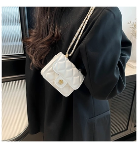 Detail of a white quilted crossbody bag featuring a gold camellia clasp and chain strap