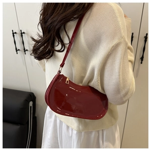 Sac à bandoulière demi-lune en cuir verni rouge porté par un mannequin de mode chic