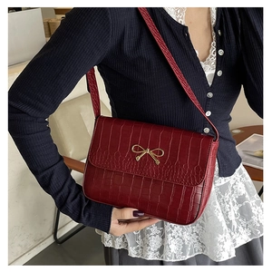 Détail de la texture crocodile bordeaux et de la boucle dorée en nœud sur le sac à main