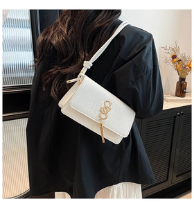 Detail showing white crocodile embossed faux leather bag with gold logo and tassel
