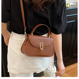 Detail of elegant brown leather handbag featuring a signature gold U-shaped metal clasp